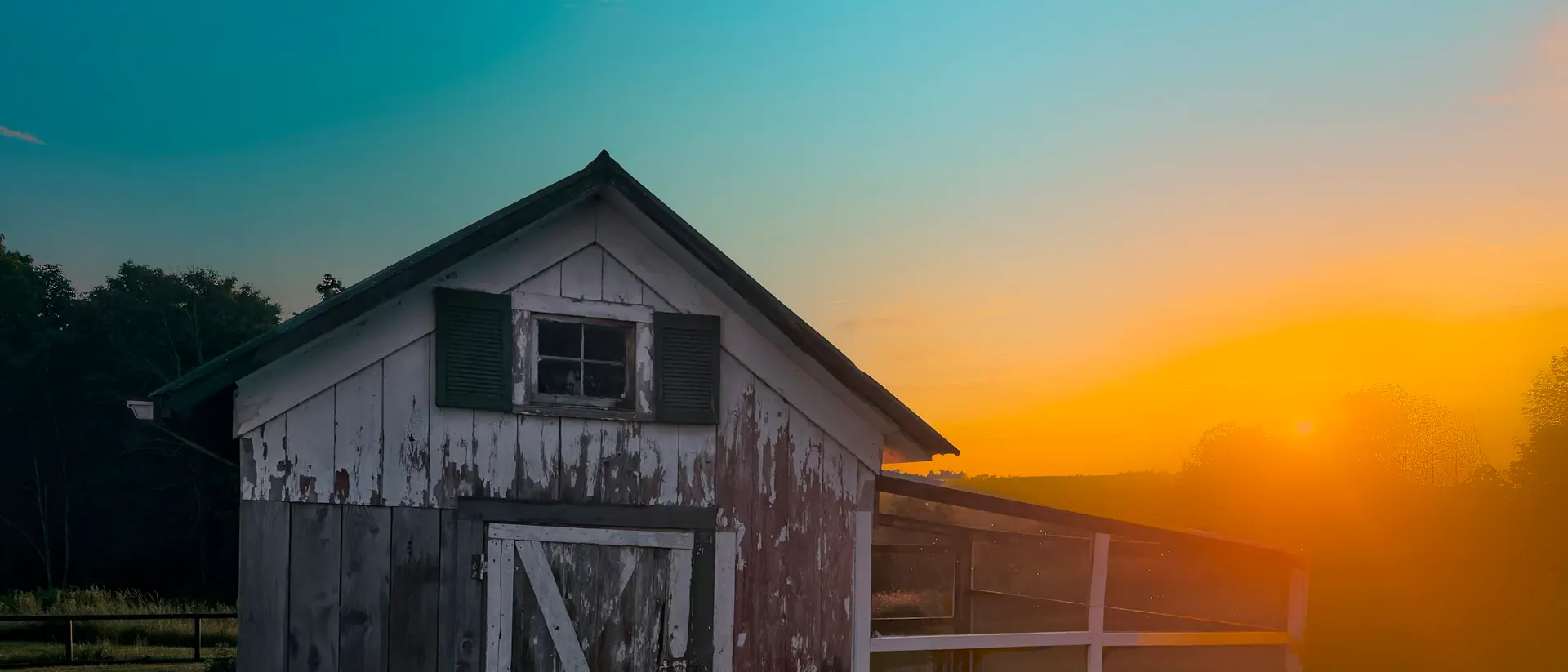 Old farm buildings beside a field at dawn, no people